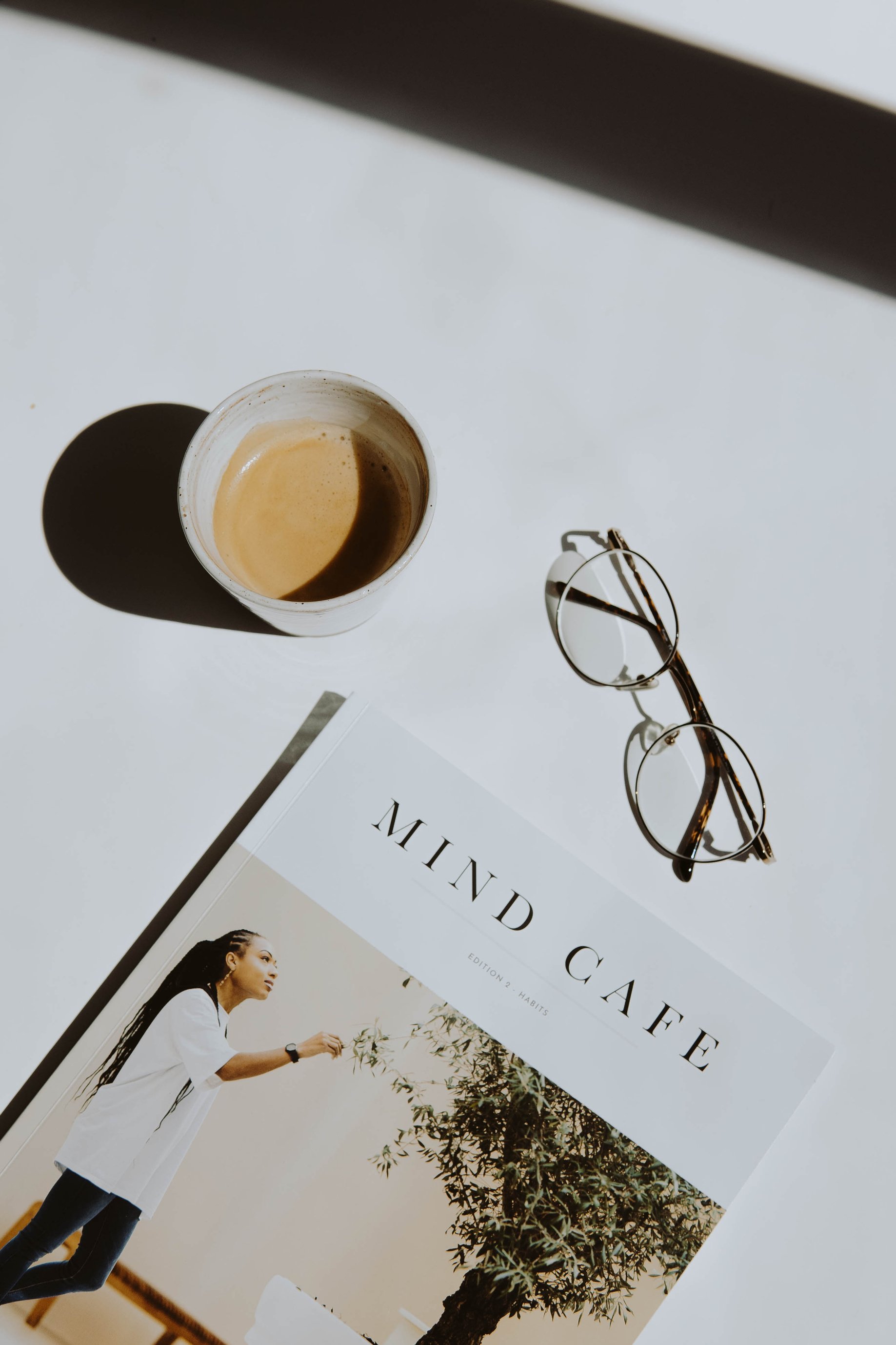 Black Framed Eyeglasses Beside White Ceramic Mug on White Table